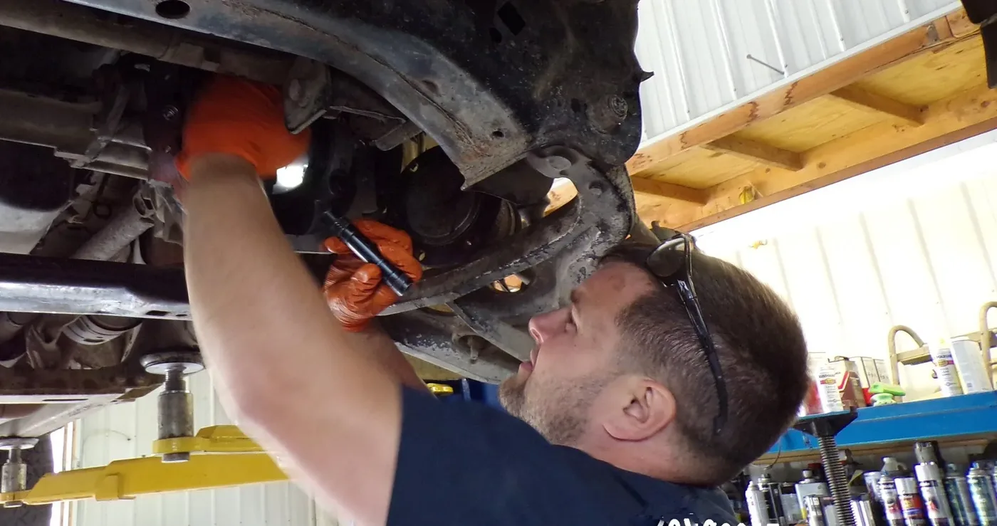 Advanced Autometric technician in safety glasses working underneath a vehicle on the lift