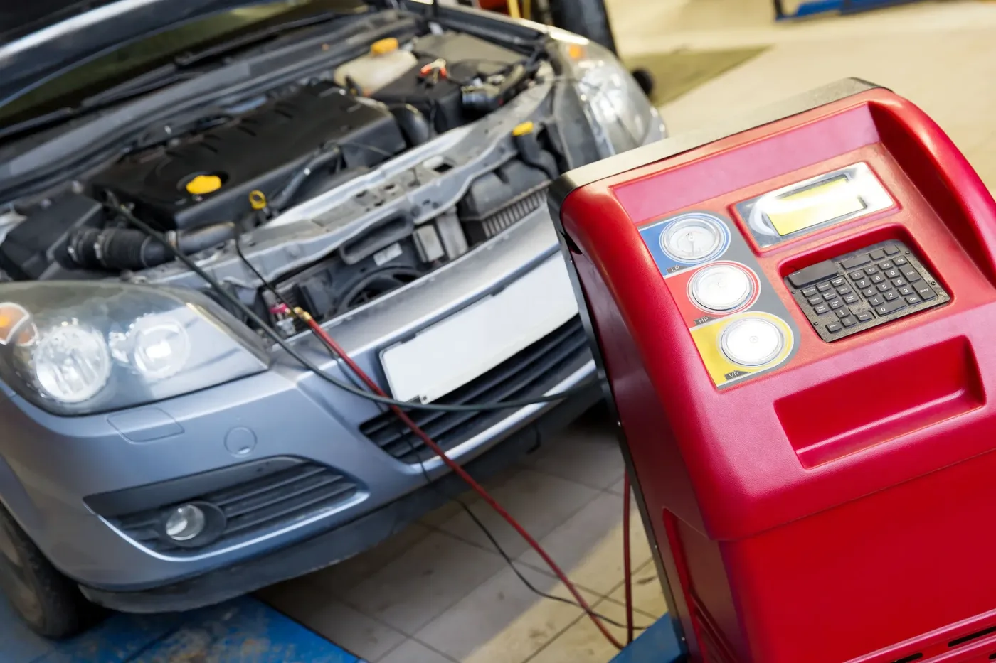 A vehicle with its hood open connected to the shop’s red air-conditioning service machine